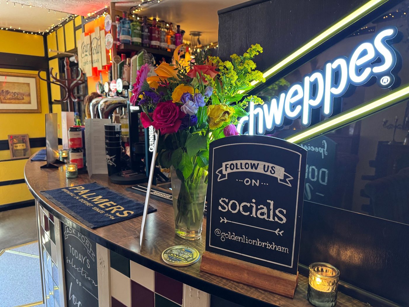 The bar: Guinness tap, Schweppes neon and a chalkboard reading follow us @goldenlionbrixham